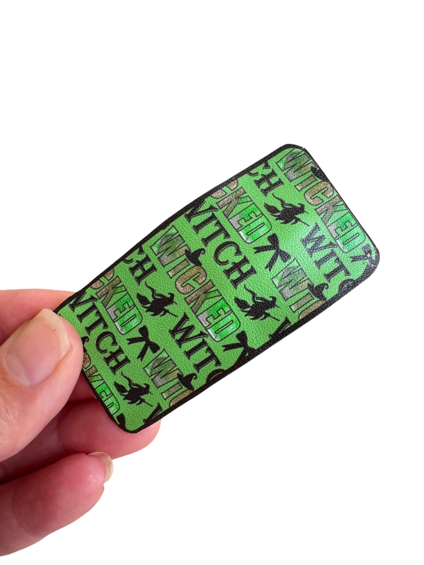 Green and black rectangular snap clip with 'Wicked Witch' text held by a hand on a white background