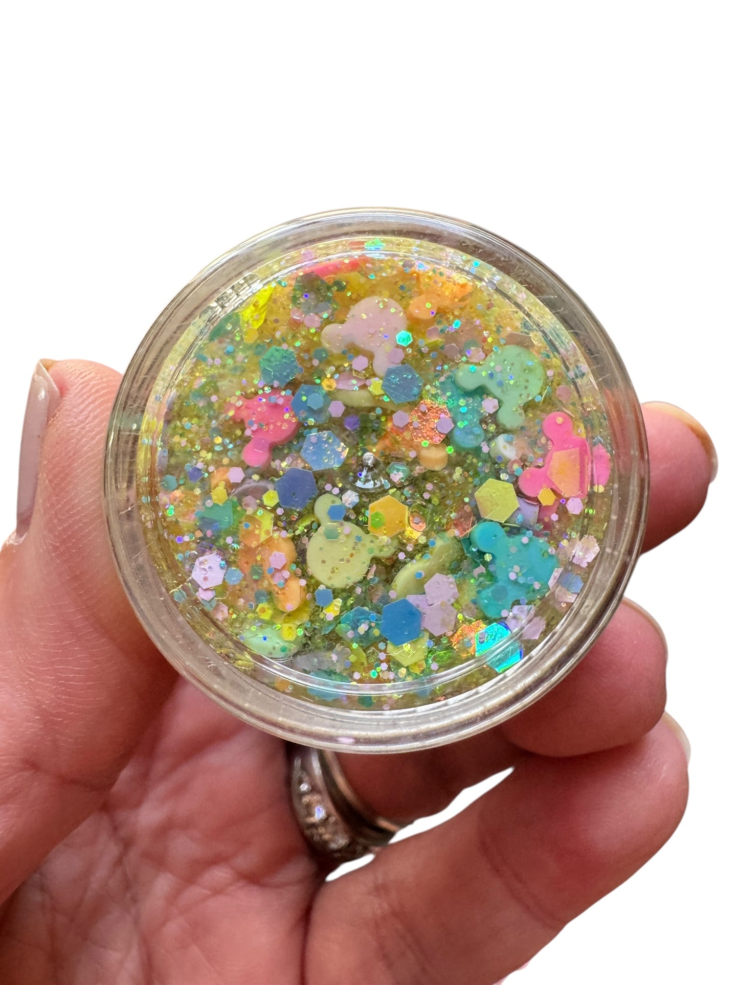 Hand holding a small jar of colorful glittery hair gel against a white background