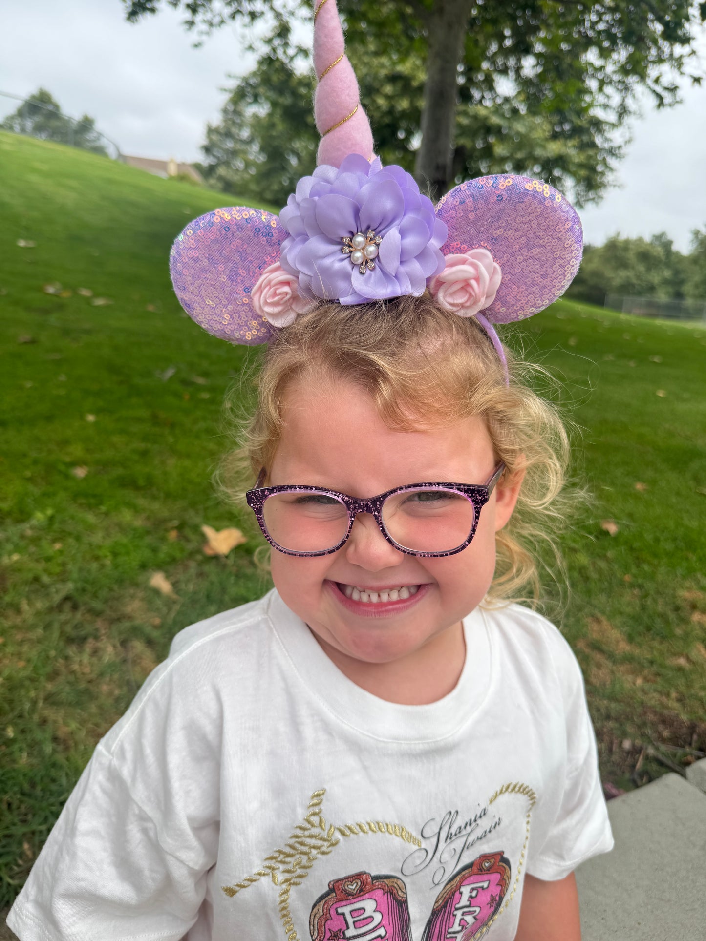 Child wearing decorative unicorn mouse ear headband and glasses outdoors