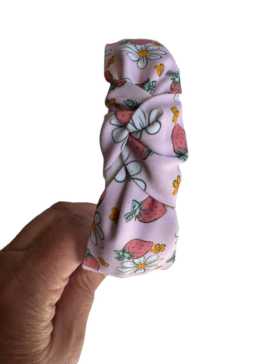 A pink headband with a floral pattern including strawberries and daisies.
