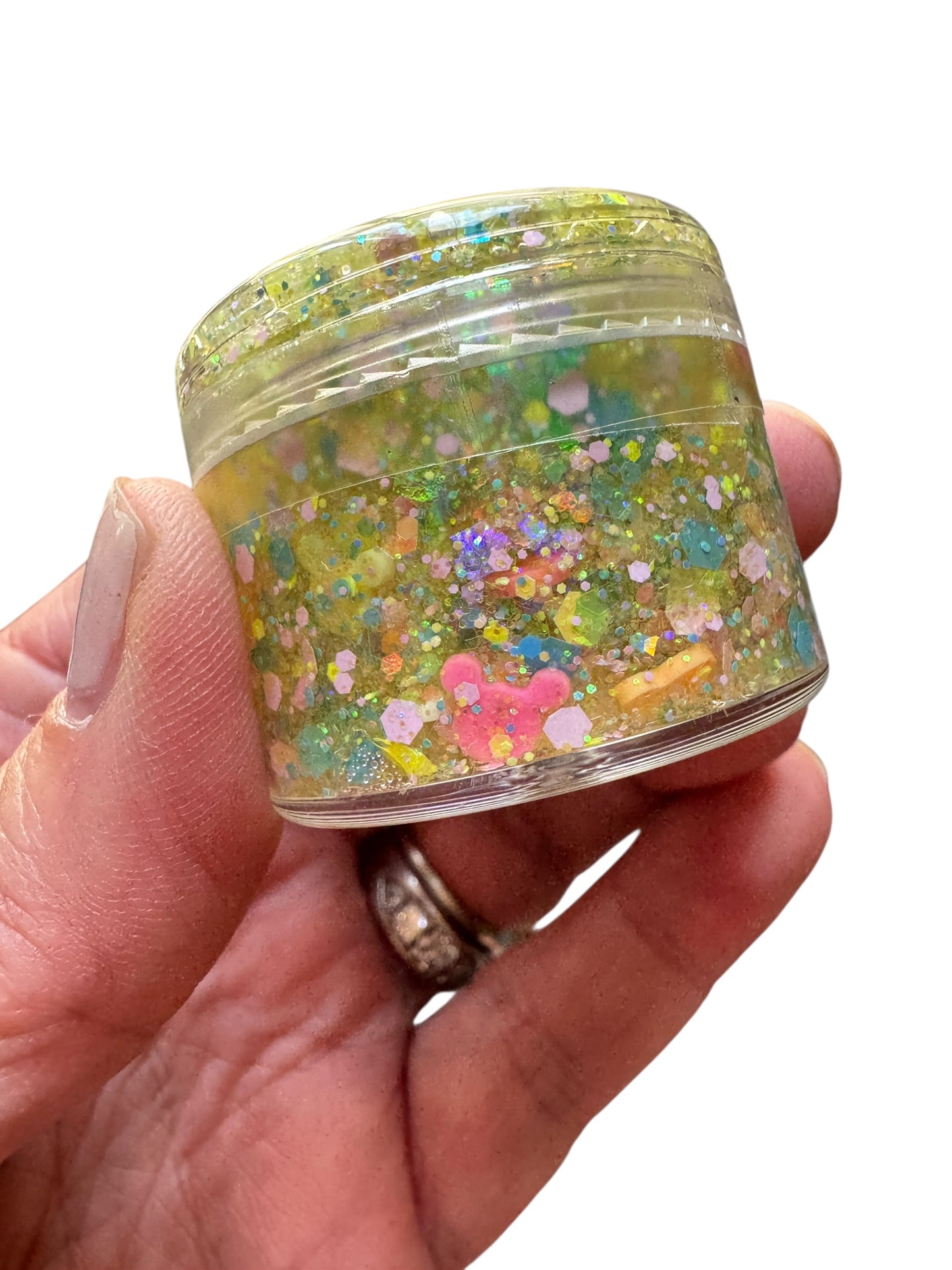 Hand holding a small jar of colorful glittery hair gel against a white background