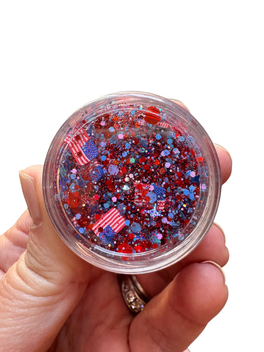 Hand holding a small container of red, blue, and white glitter.