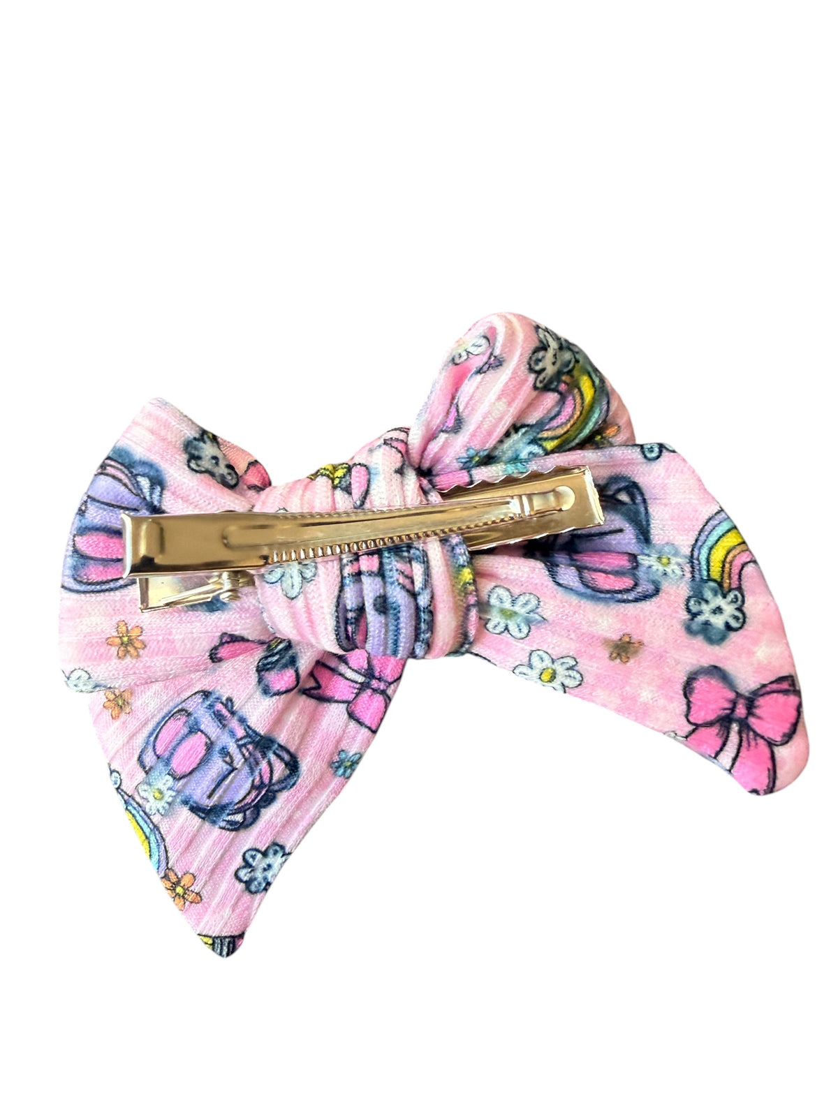 A pink fabric hair bow clip with a colorful retro pattern of umbrellas, rainbows, and flowers, secured with a gold-tone metal bar, shown on a plain white background.