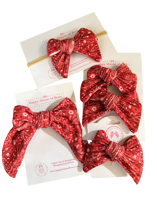 A set of four red patterned hair accessories from Happy House of Bowls, including two large fabric hair bows, one small hair bow on a elastic band, and one matching scrunchie, all displayed on their white paper packaging cards against a white background.