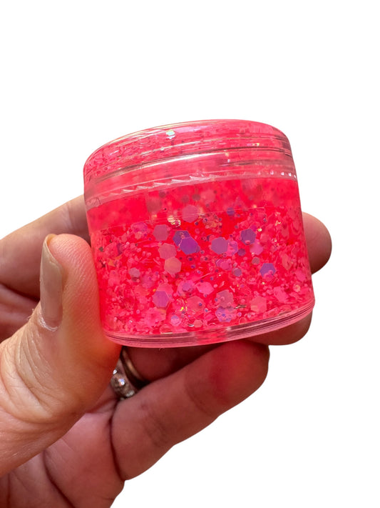 Hand holding a small container of pink glittery slime against a white background