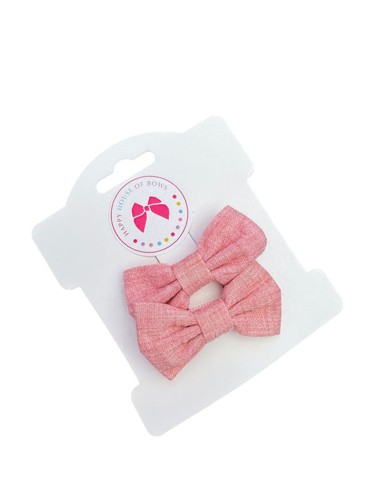 A set of two pink linen baby hair clips attached to a plastic display card.