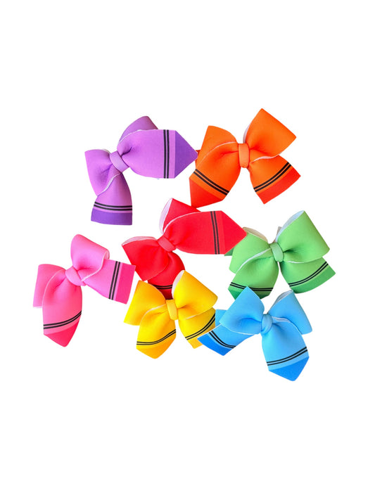 A set of nine colorful hair bows shaped like crayons, arranged in a cluster on a solid white background. The bows feature vibrant colors including purple, orange, pink, red, yellow, green, and blue, each with thin black stripe details at the ends.