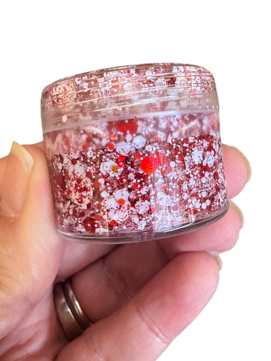 Hand holding a small container of red and white glitter hair gel  with baseballs