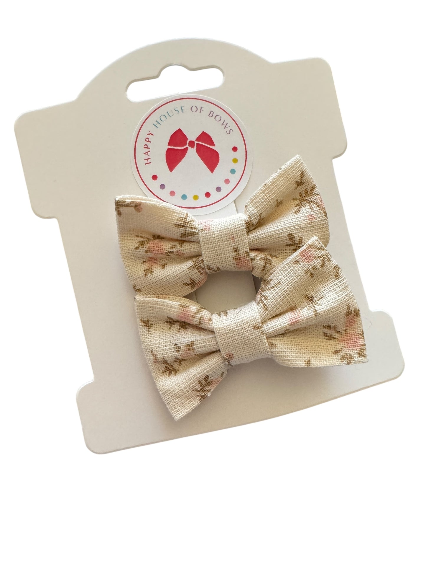 Two beige floral-patterned hair bows on a white card with 'Happy House of Bows' branding.