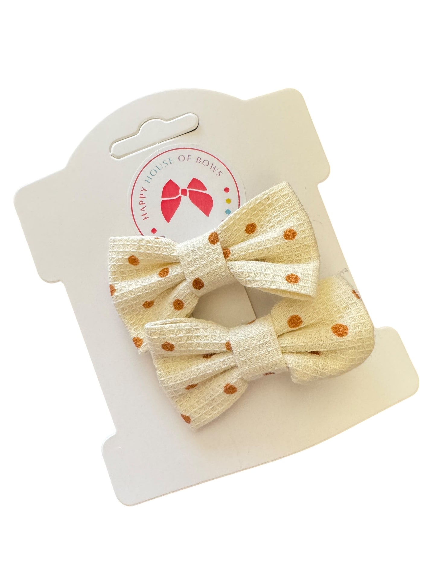 Set of two beige polka dot hair bows on a white card with brand logo.