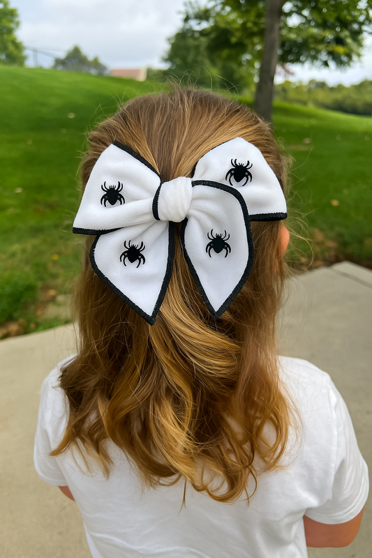 girl with a large white hair bow featuring black spider designs outdoors.