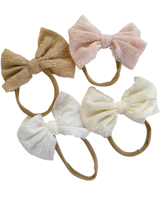 Set of four hair bows in beige, pink, white, and cream on a white background