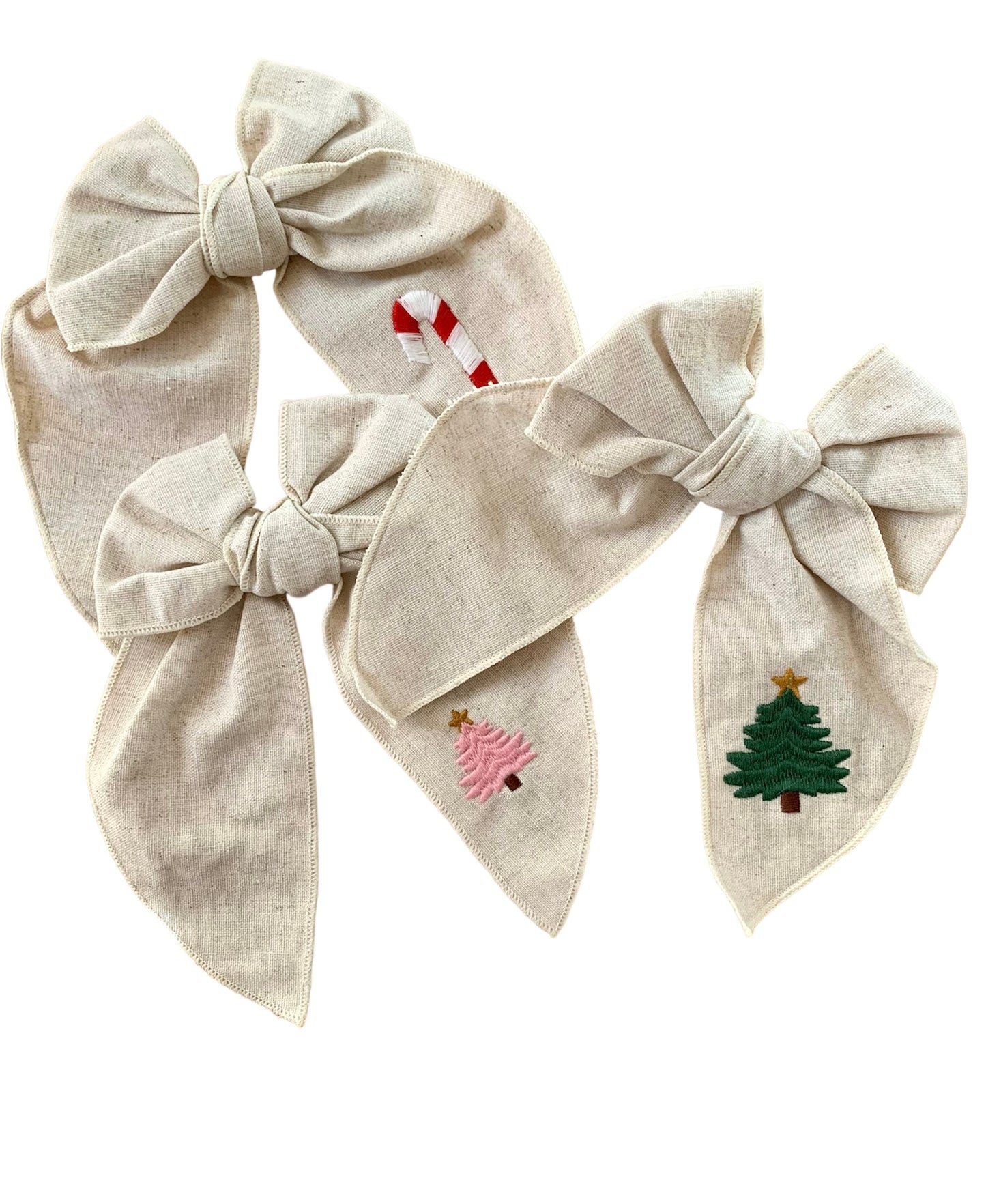 A beige linen hair bow with a Christmas tree, and candy cane embroidery on it, attached to an alligator clip.