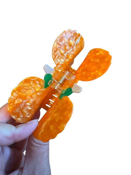 An orange pumpkin-shaped Halloween mouse ear claw clip held in a hand against a white background