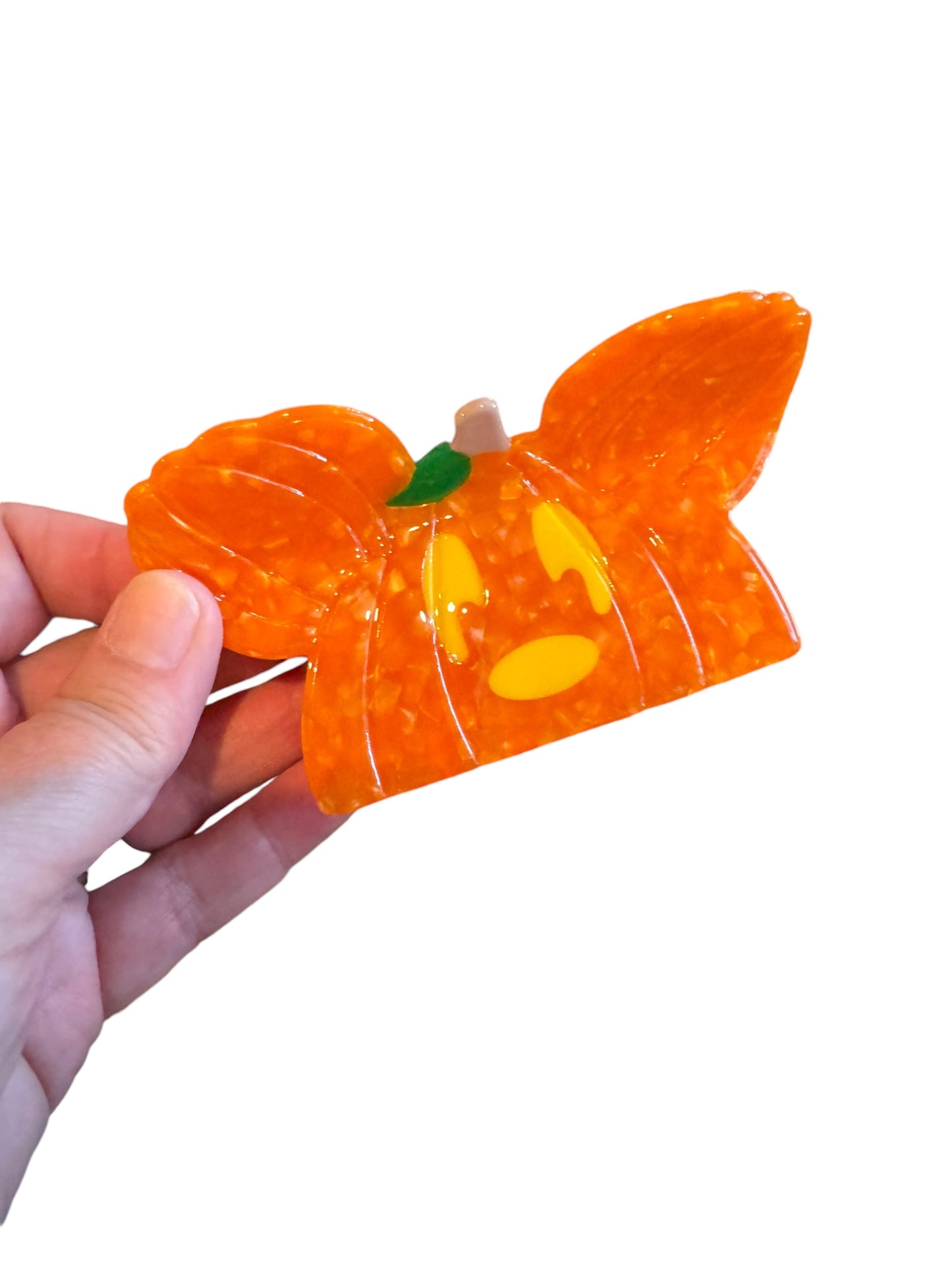 An orange pumpkin-shaped Halloween mouse ear claw clip held in a hand against a white background