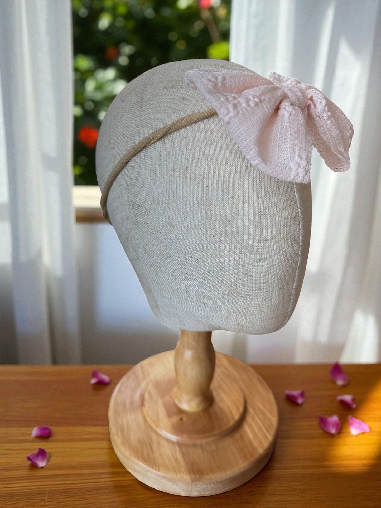 Headband with a pink bow on a mannequin head against a blurred outdoor background