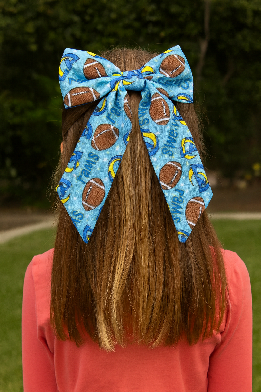 Person wearing a large blue hair bow with football and sports designs outdoors.