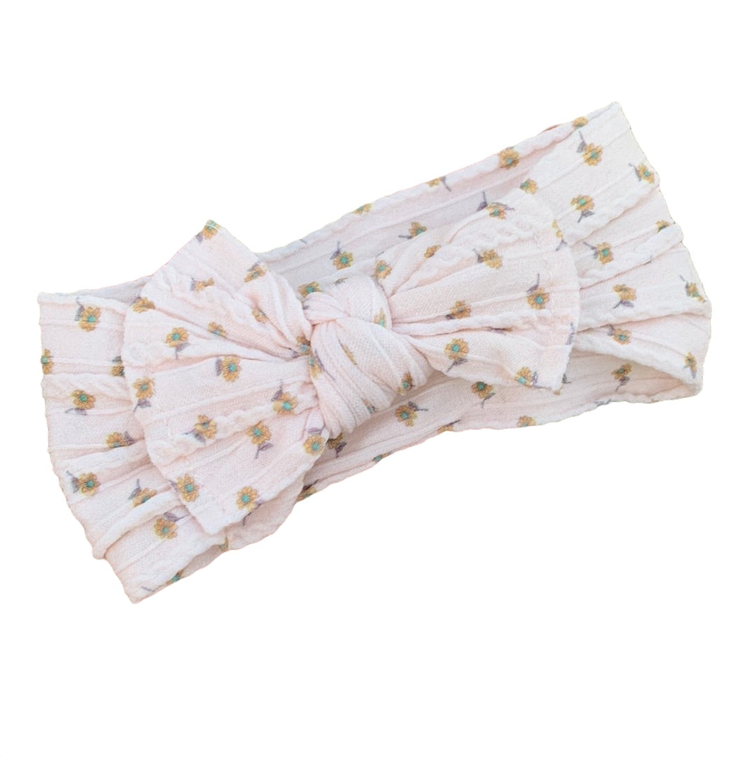 A neutral floral patterned nylon headband for babies with large bow