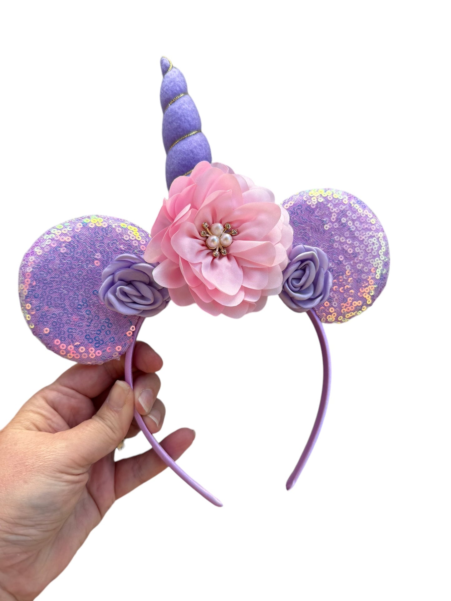 purple and pink unicorn mouse ear headband in a hand with pink rhinestone flower