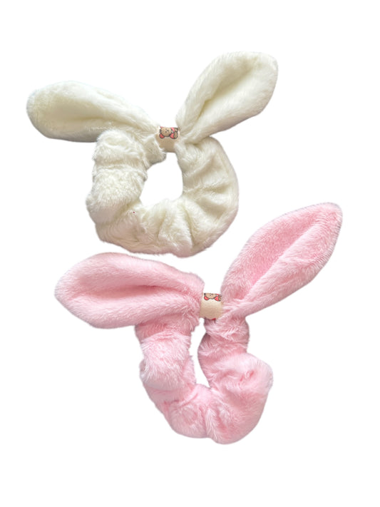 Two bunny ear scrunchies, one in white and one in pink, against a white background.