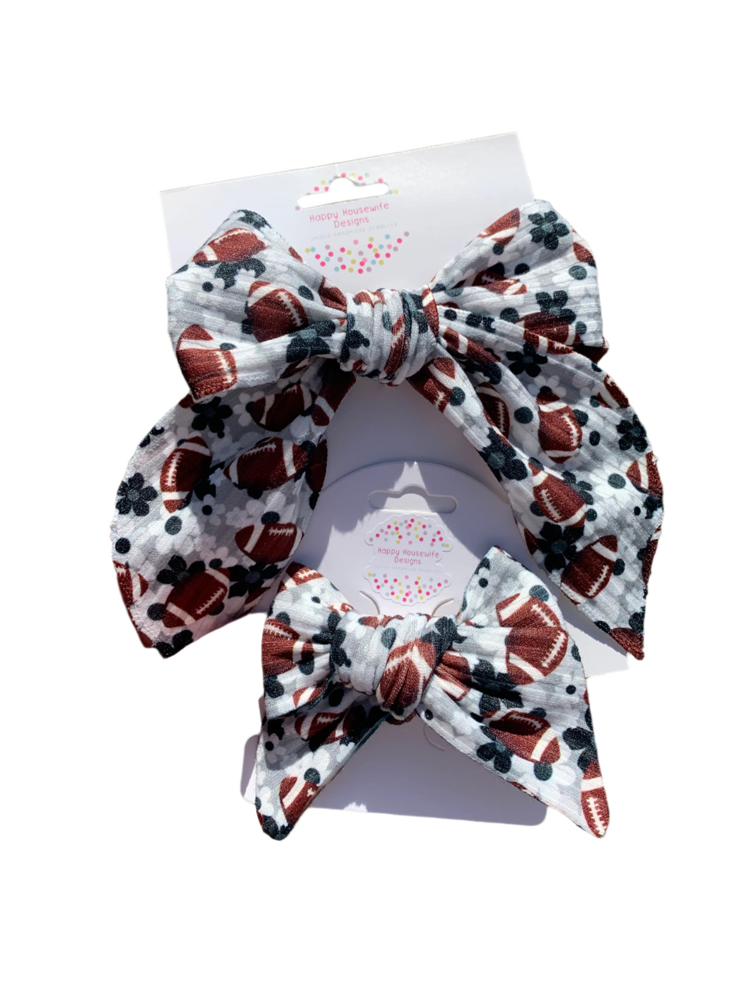 A hand holding a hair bow with a floral and football pattern on it, displayed against a grassy background.