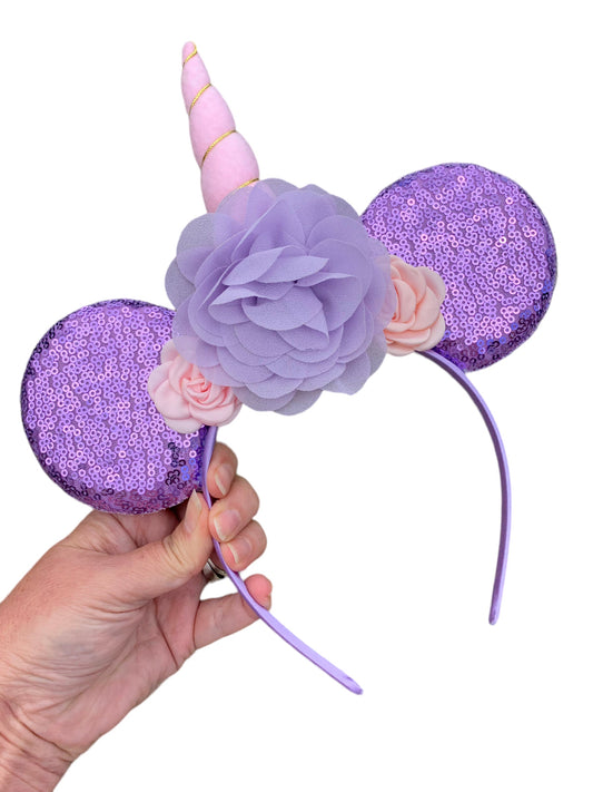 purple and pink unicorn mouse ear headband in a hand