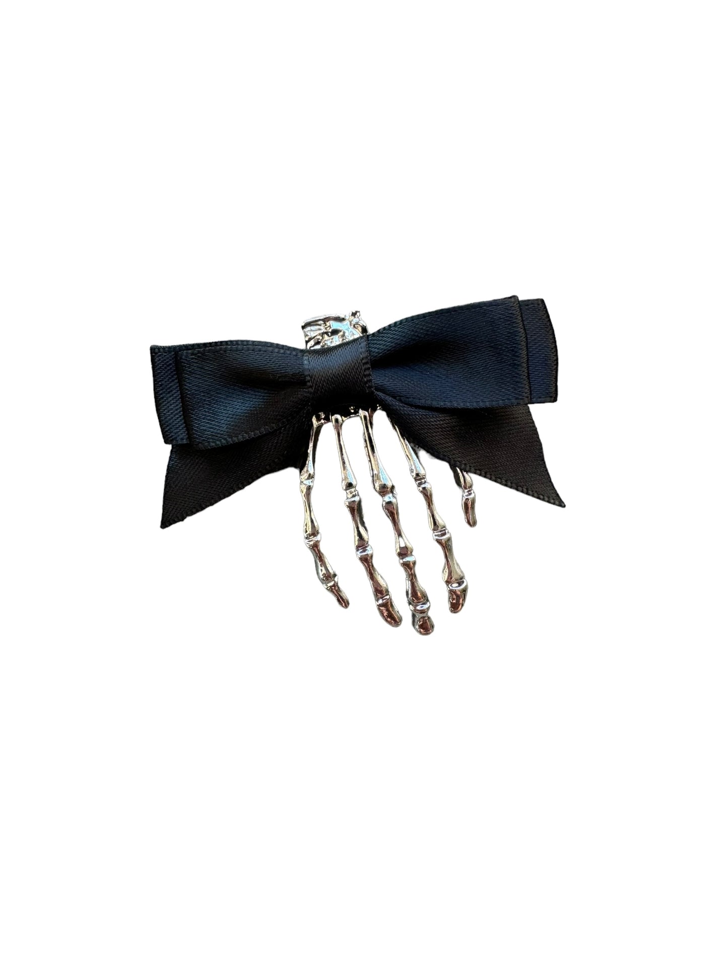 A hand holding a skeleton hair clip with a black bow and metal skeleton design.