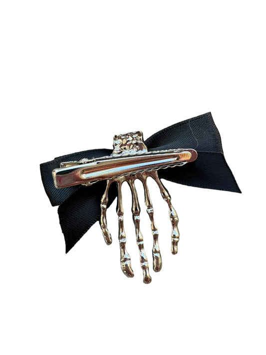 A hand holding a skeleton hair clip with a black bow and metal skeleton design.