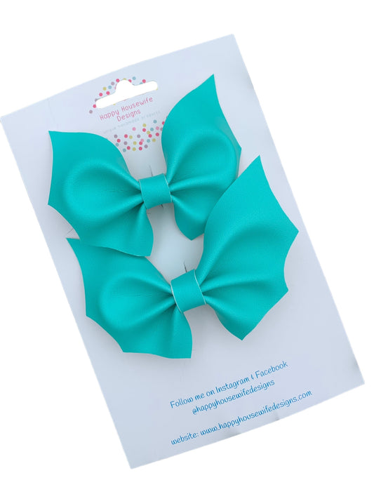 A set of faux leather hair bows in various colors with an alligator clip attached, displayed on a card.