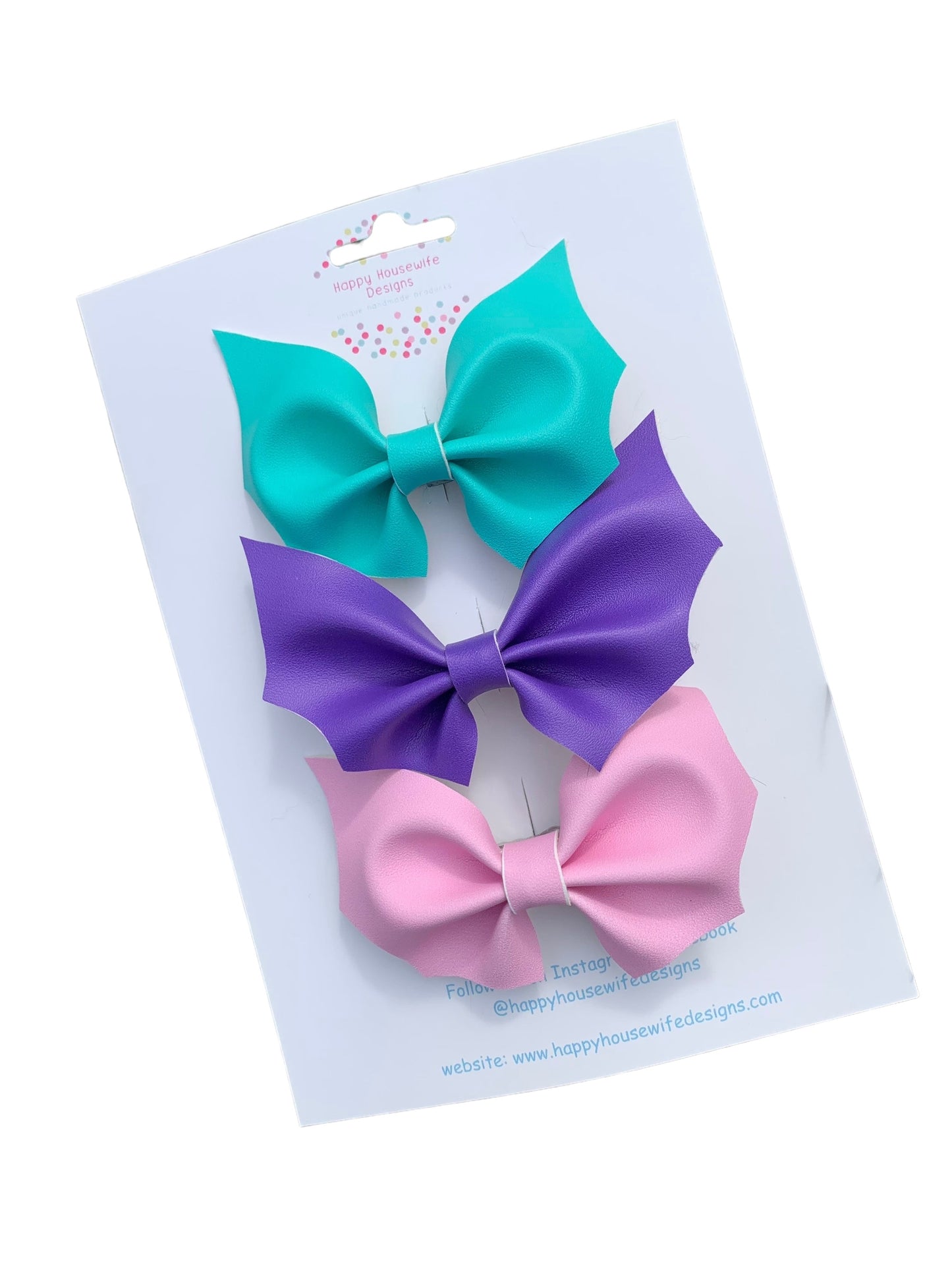 A set of faux leather hair bows in various colors with an alligator clip attached, displayed on a card.