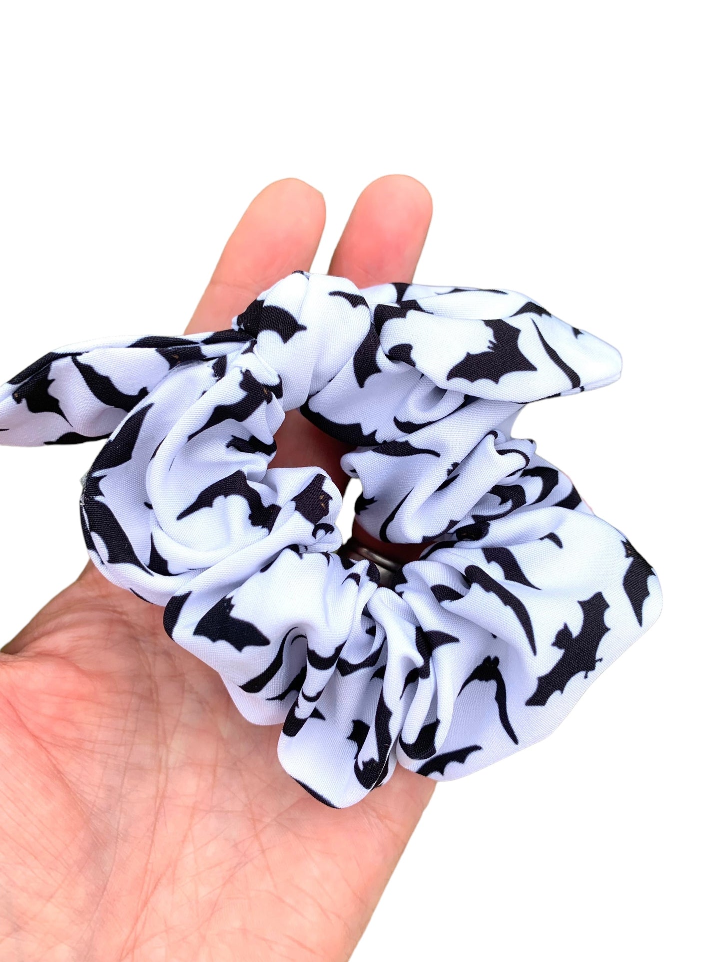 A hand holding a hair bow with a white background and black bat patterns, with a tie knot headband.