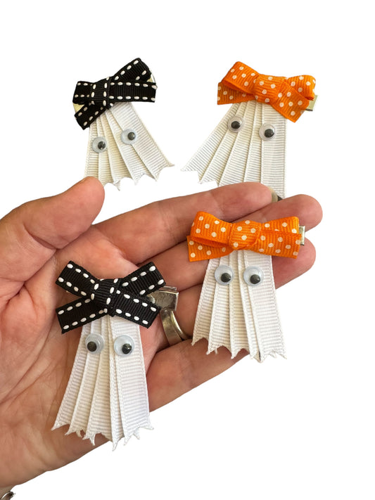 A hand holding three Ribbon Ghost Hair Bows with black and orange ribbons on a white background.