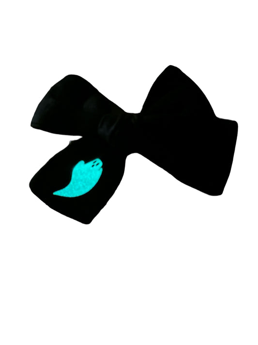 A black hair bow with a glowing blue ghost design, attached to an alligator clip, against a white background.