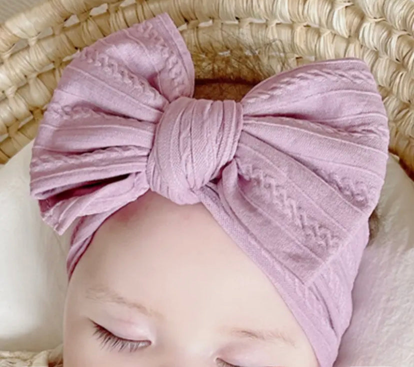 A baby wearing a lavender-colored nylon headwrap with a big bow.