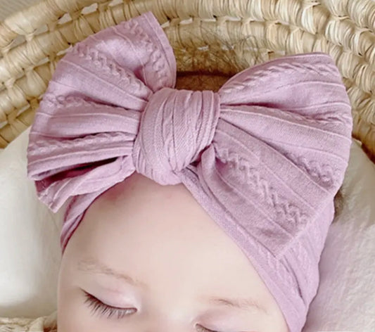A baby wearing a lavender-colored nylon headwrap with a big bow.