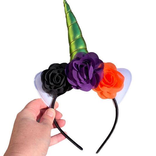 A hand holding a unicorn headband with a green horn and flowers in black, purple, and orange.