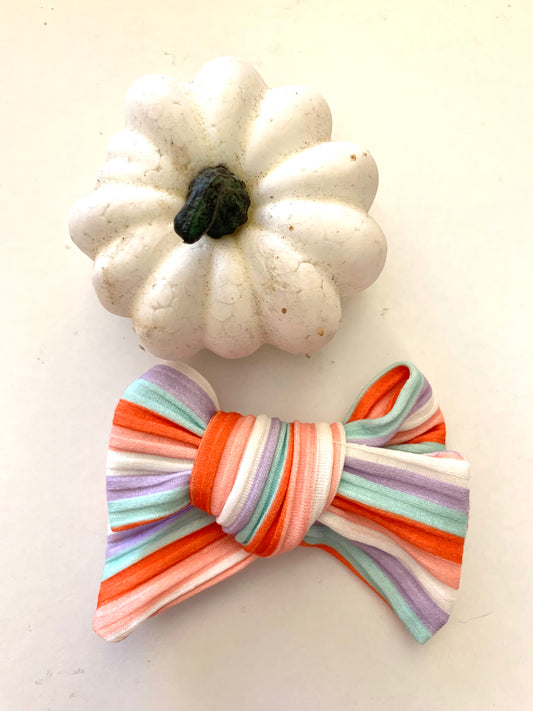 hair bow with fall striped patterns, one in orange and the other in purple, displayed on a white surface with a small white pumpkin in the background.