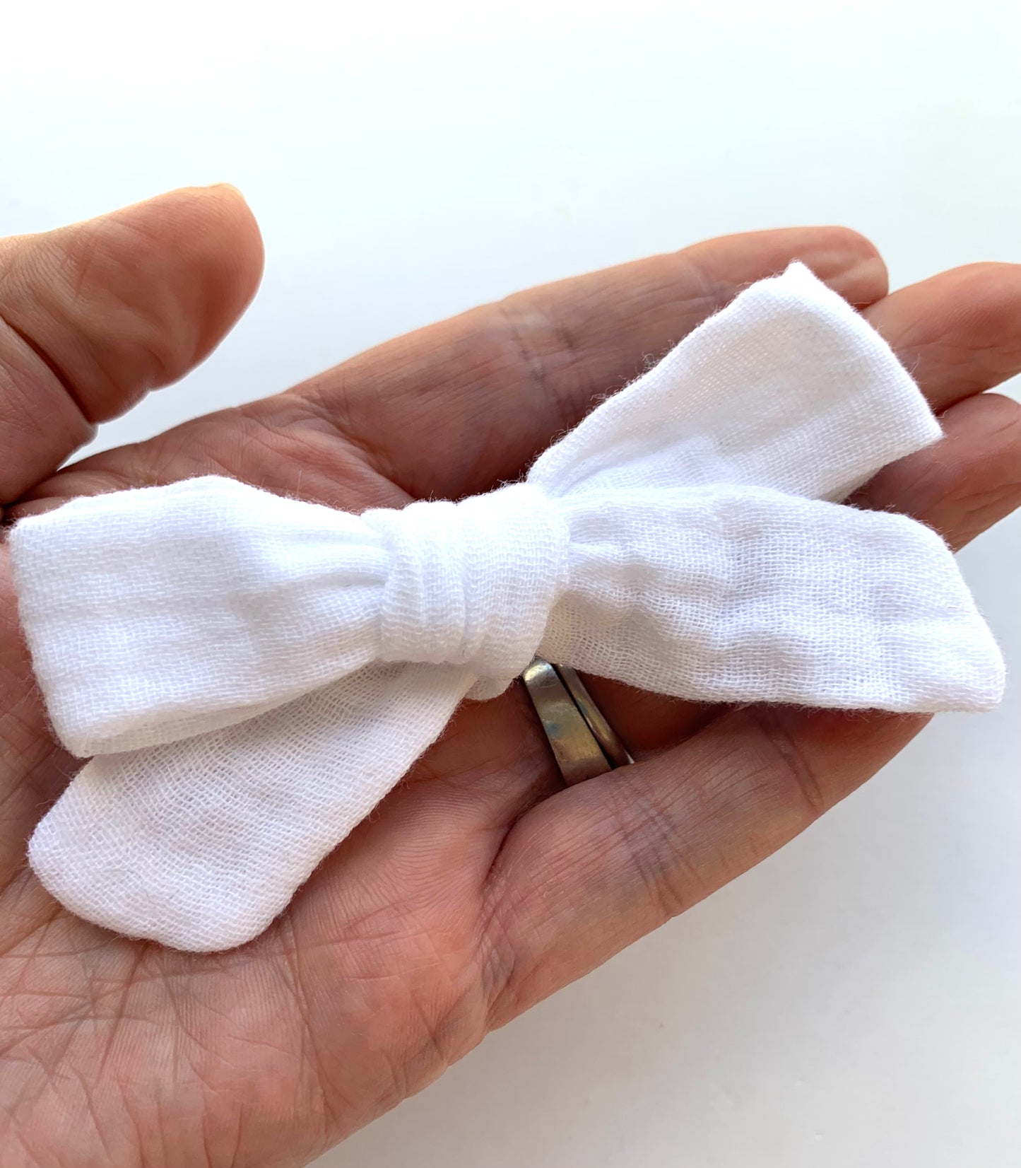A hand holding a white mini Muslin hair bow clip.