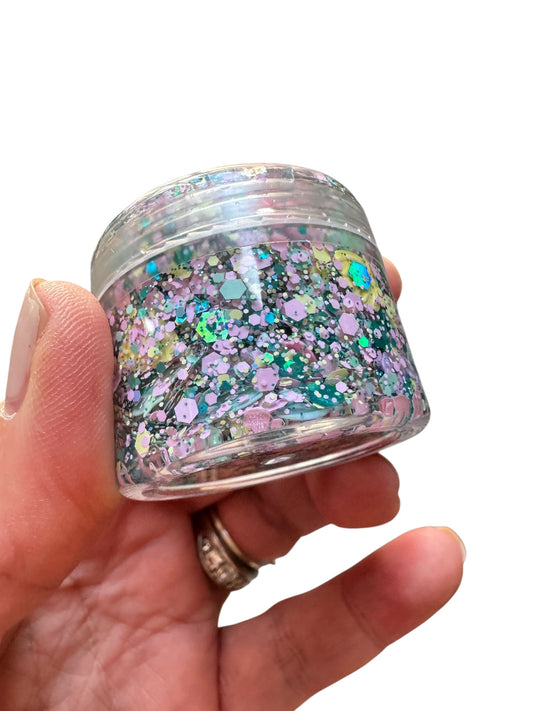 Clear container filled with mermaid hair glitter  gel held in a hand on a white background