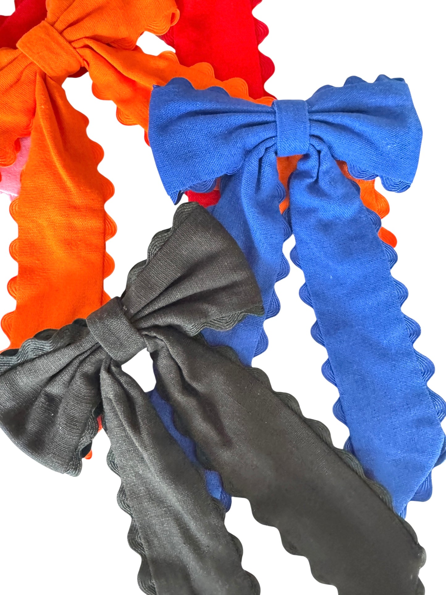 Three hair bows in orange, blue, and black on a white background