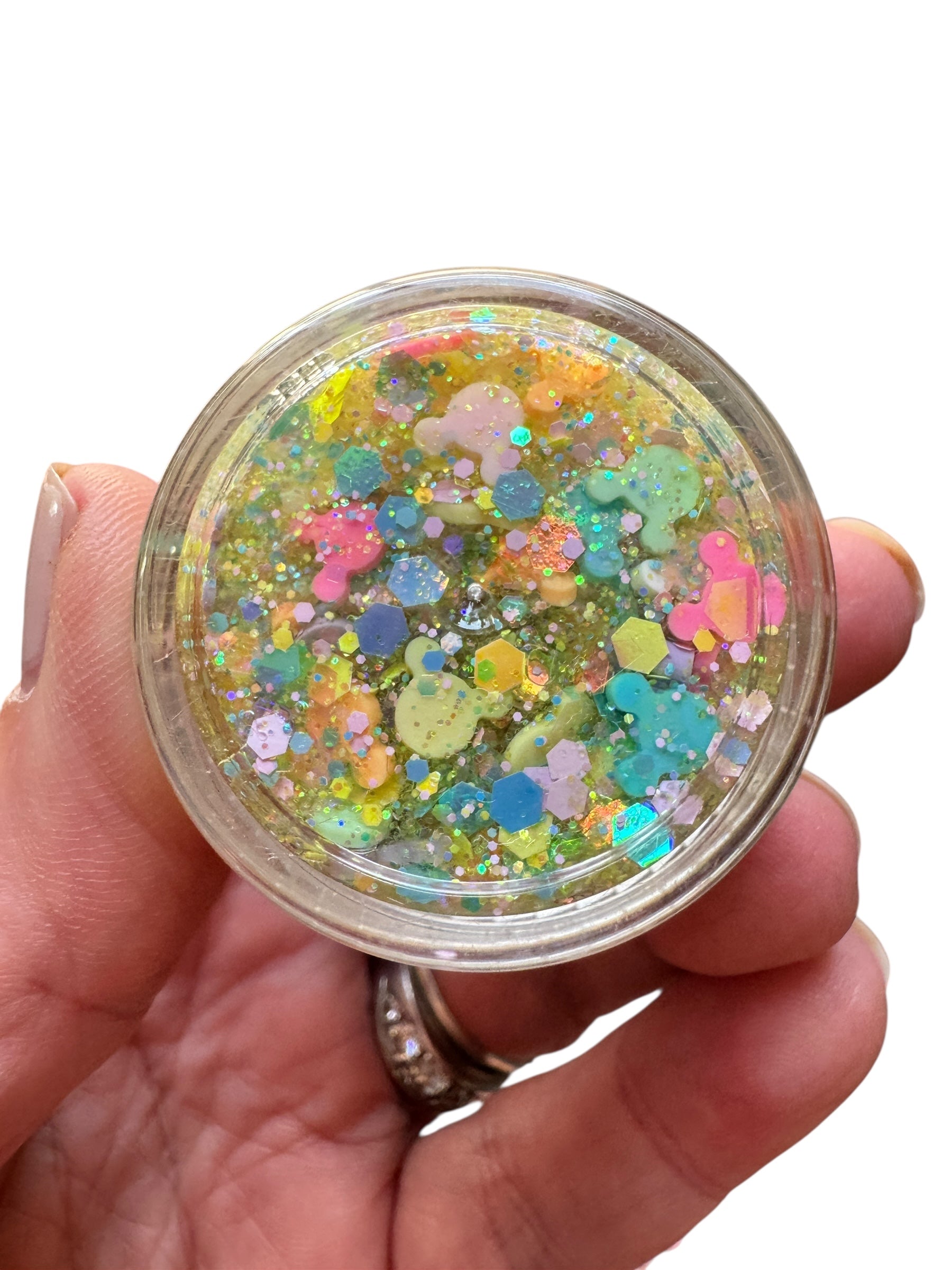 Hand holding a small jar of colorful glittery hair gel against a white background