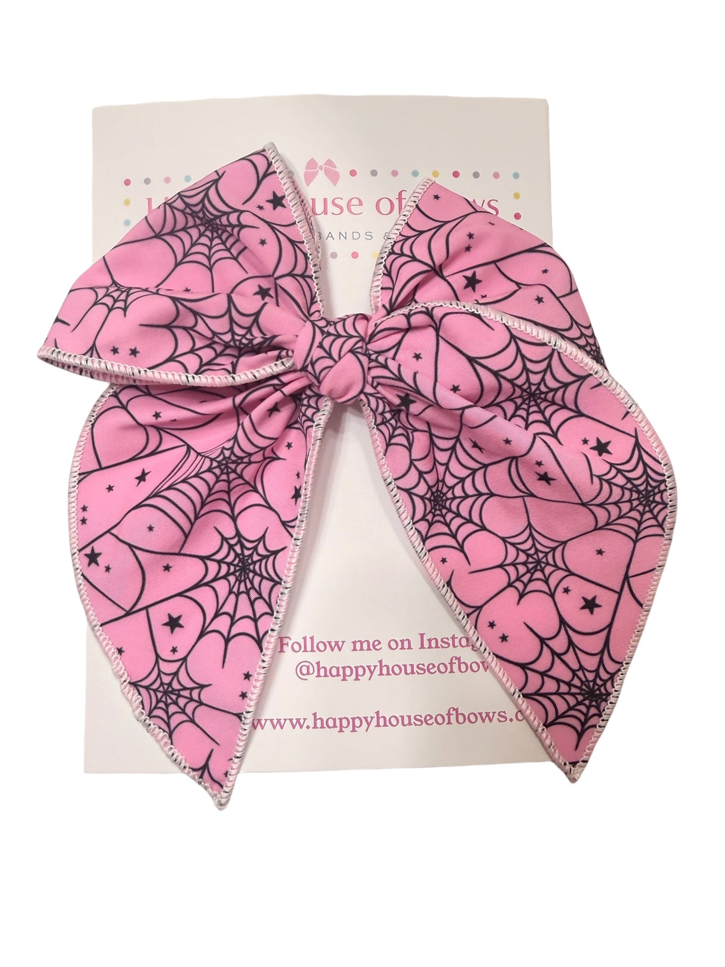 A large pink hair bow with a black spiderweb and heart pattern, displayed on a white backing card from Happy House of Bow.