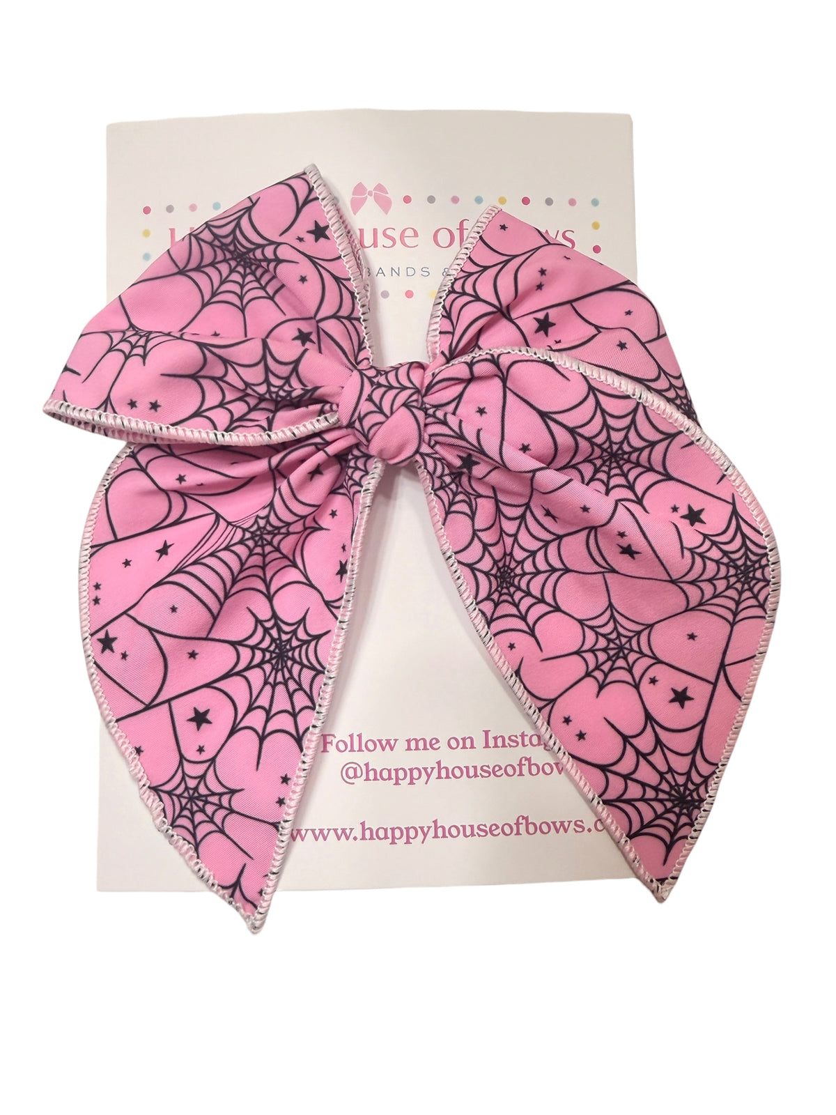 A large pink hair bow with a black spiderweb and heart pattern, displayed on a white backing card from Happy House of Bow.
