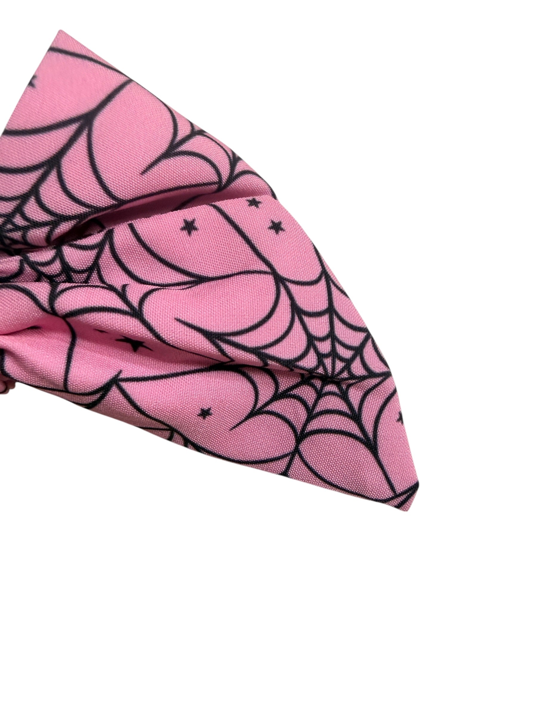 A pink fabric hair bow, featuring a black spiderweb and star pattern, shown on a plain white background.