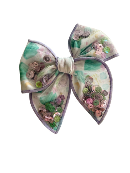 A large hair bow featuring a pastel green and lavender watercolor pattern, embellished with sequins and beads, set against a plain white background.