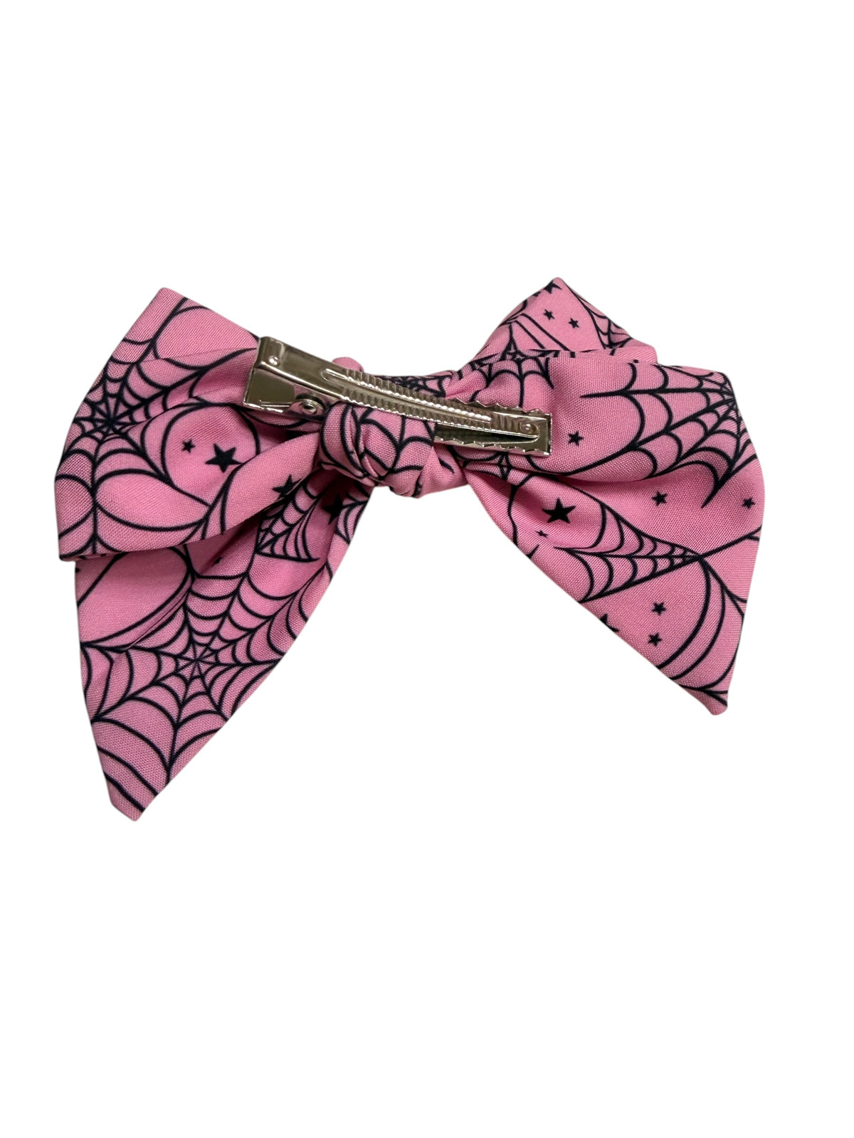 A pink hair bow with a black spiderweb and star pattern, secured with a silver metal clip, shown against a plain white background.