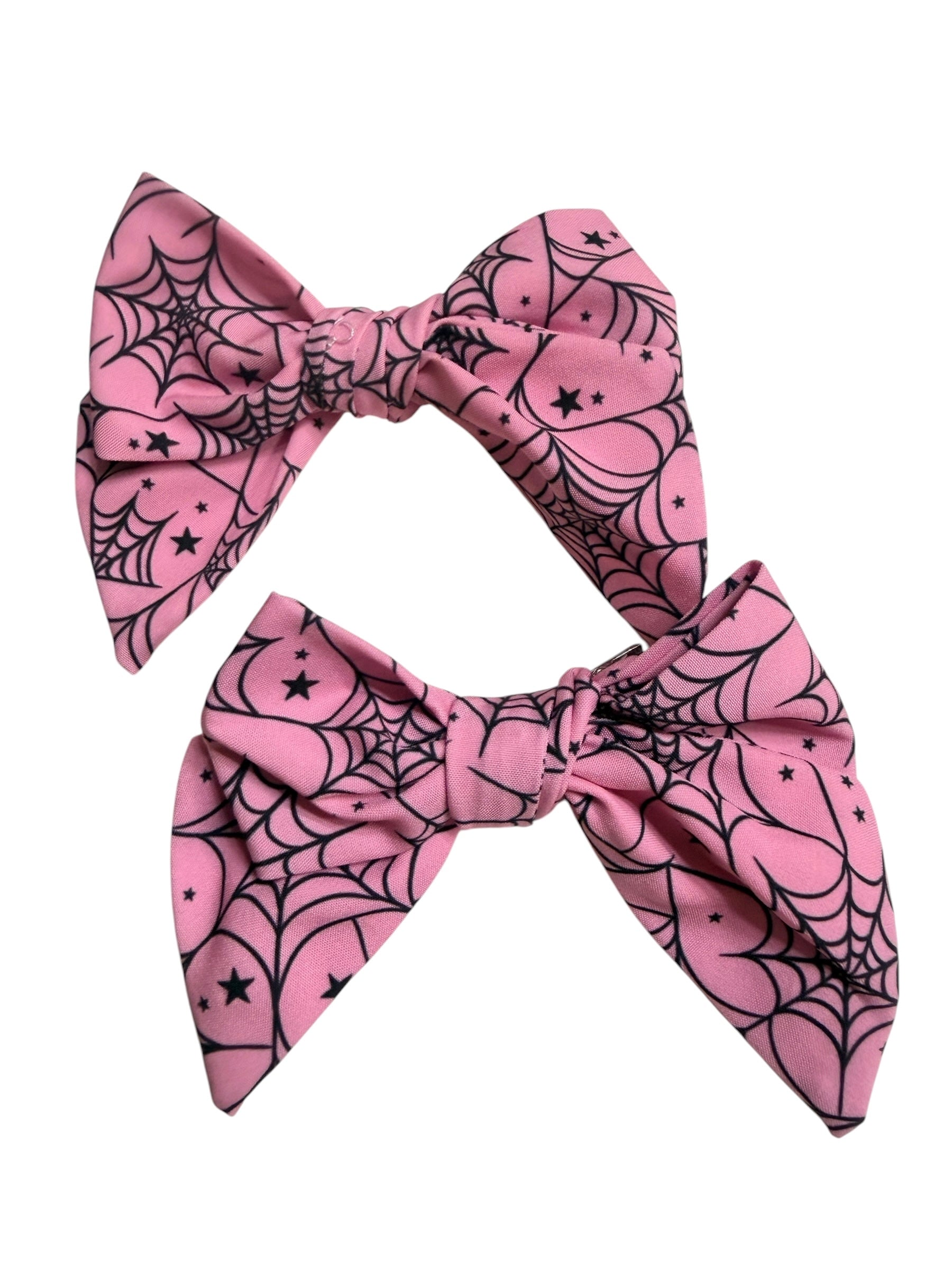Two pink fabric hair bows with a black spiderweb and star pattern, displayed against a plain white background.