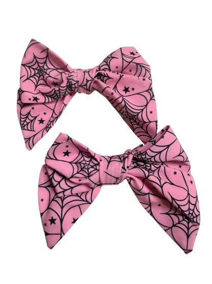 Two pink fabric hair bows with a black spiderweb and star pattern, displayed against a plain white background.
