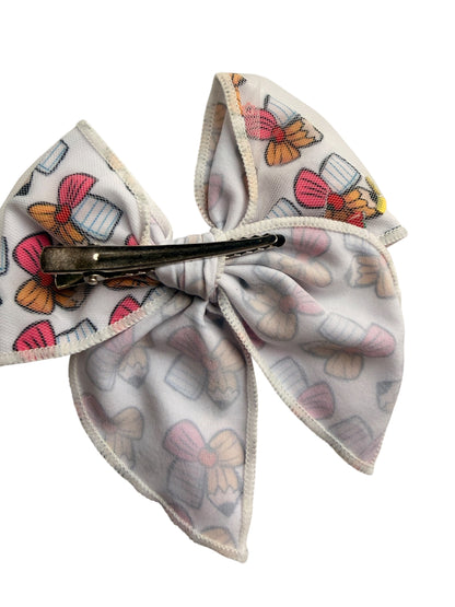 A fabric hair bow clip with a white background and a colorful print of butterflies and bows, secured with a black metal claw clip.