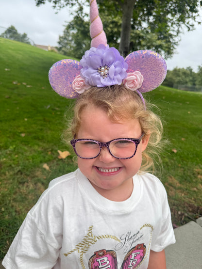 Child wearing decorative unicorn mouse ear headband and glasses outdoors